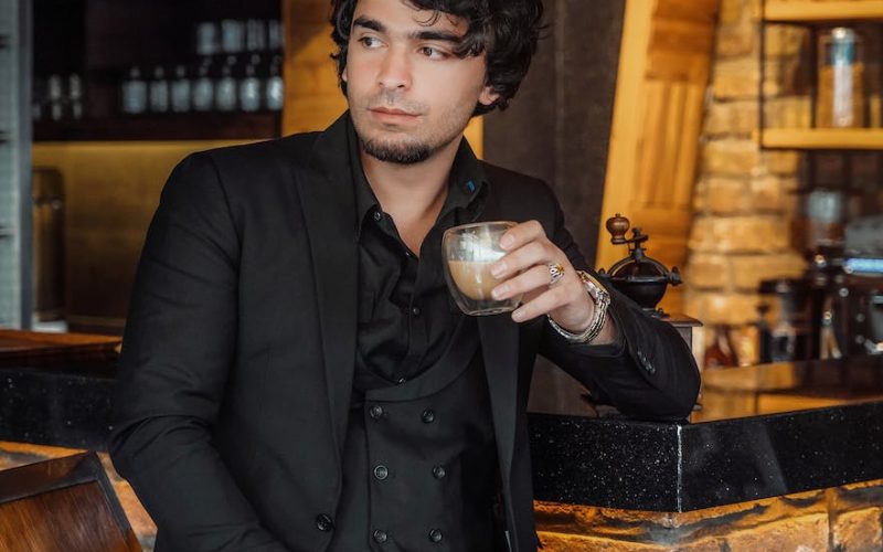 man in black suit jacket holding glass of coffee